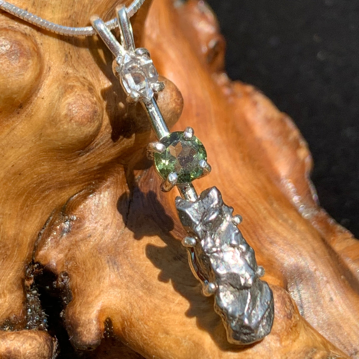 sterling silver pendant necklace with Herkimer diamond, moldavite, and campo del cielo meteorite sits on driftwood for display