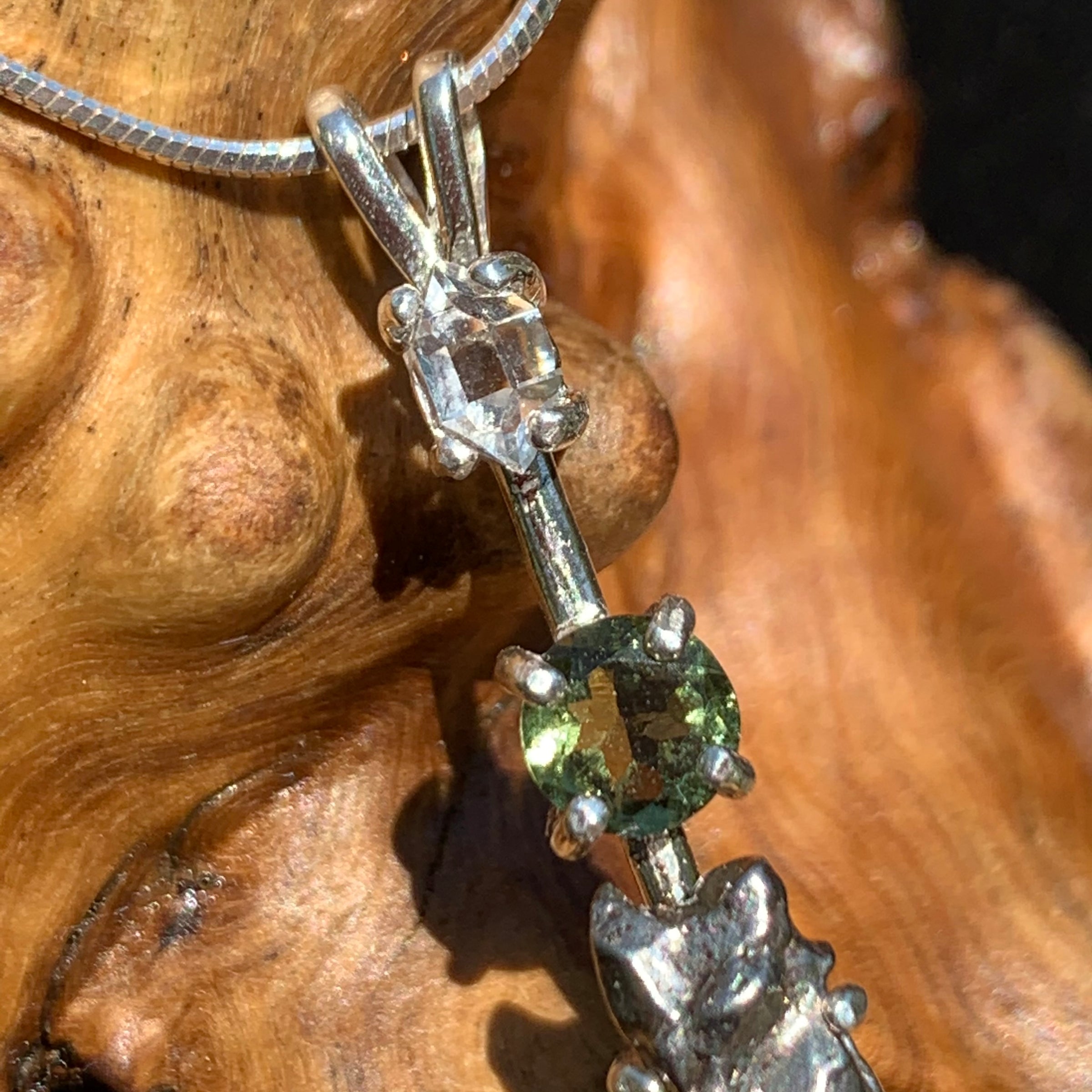 close up view of sterling silver pendant necklace with Herkimer diamond, moldavite, and campo del cielo meteorite sitting on driftwood for display