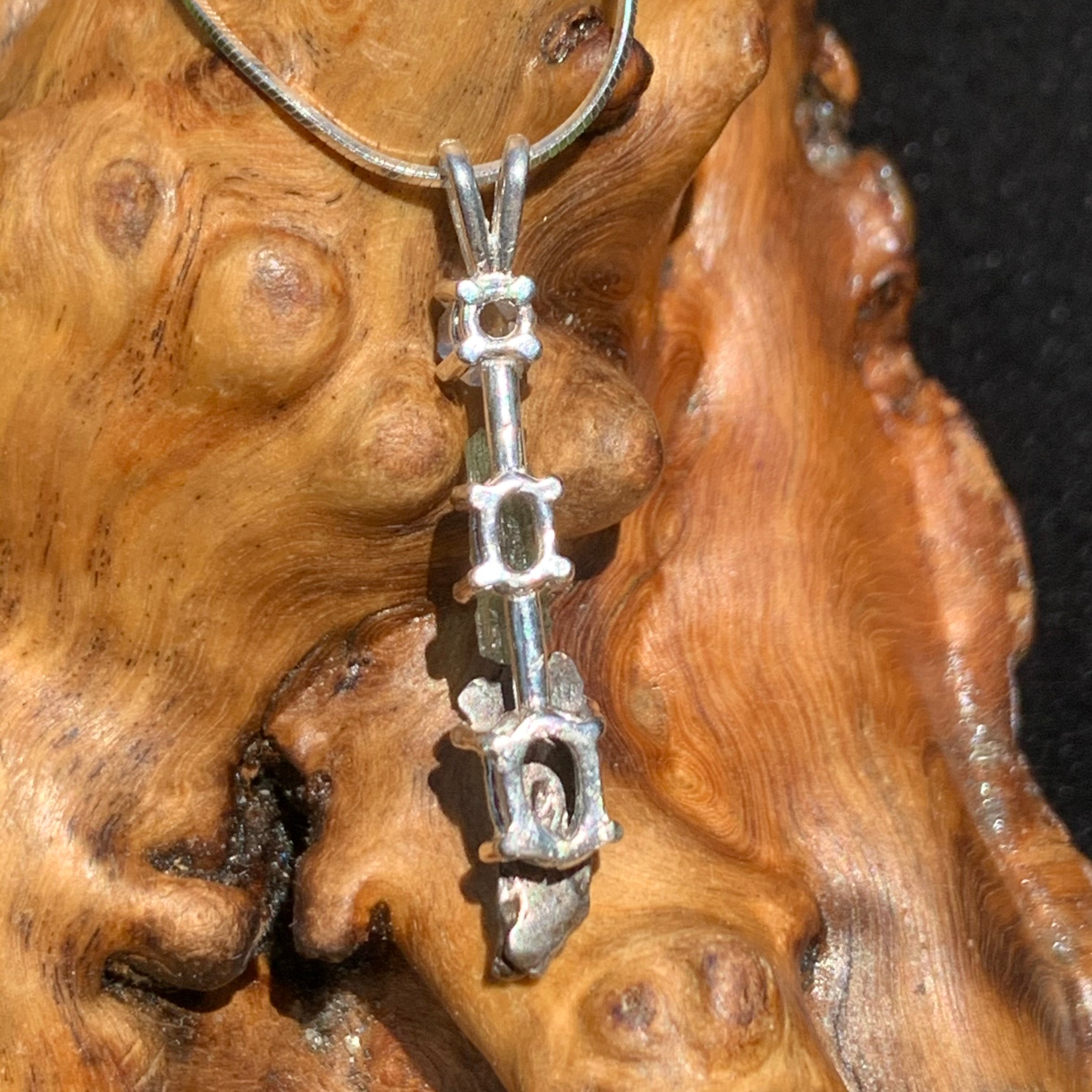back side view of a sterling silver pendant necklace with Herkimer diamond, moldavite, and campo del cielo meteorite sitting on driftwood for display