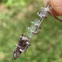 sterling silver pendant necklace with Herkimer diamond, moldavite, and campo del cielo meteorite is held up to show details