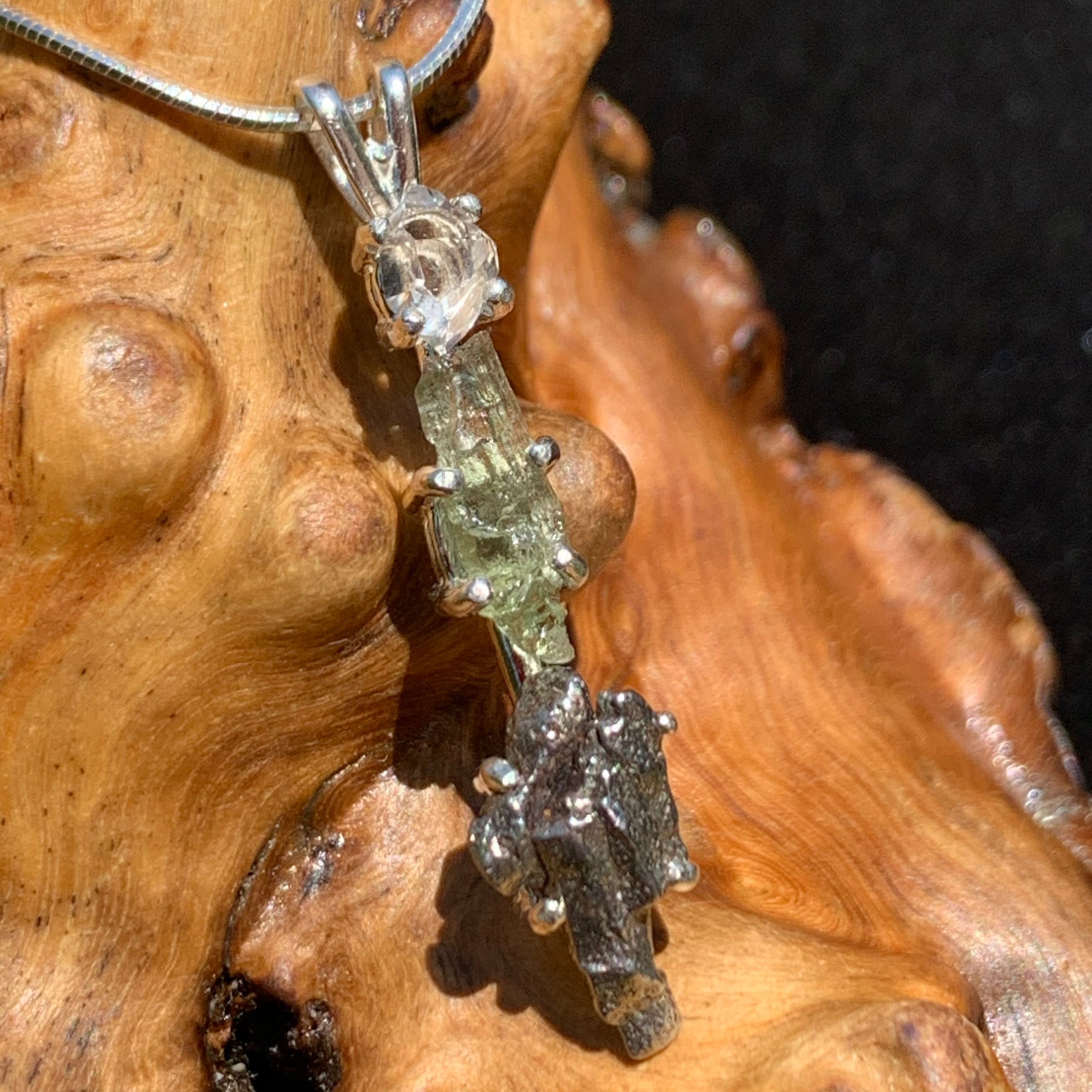 sterling silver pendant necklace with Herkimer diamond, moldavite, and campo del cielo meteorite sitting on driftwood for display