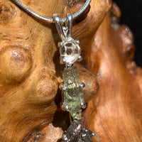 close up view of a sterling silver pendant necklace with Herkimer diamond, moldavite, and campo del cielo meteorite sitting on driftwood for display