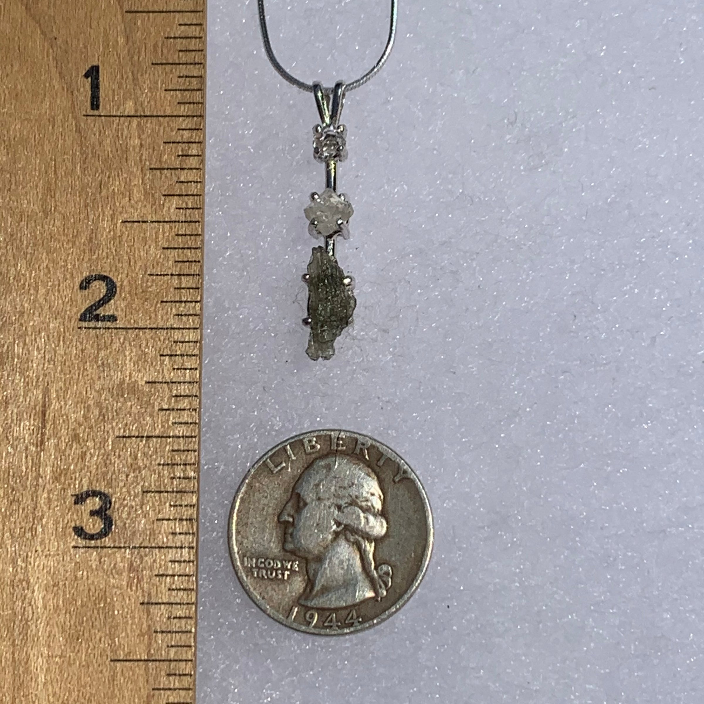 sterling silver pendant necklace with Herkimer diamond, moldavite, and phenacite next to a ruler and a US quarter for scale