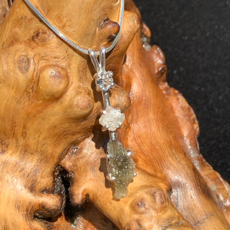 sterling silver pendant necklace with Herkimer diamond, moldavite, and phenacite sitting on driftwood for display