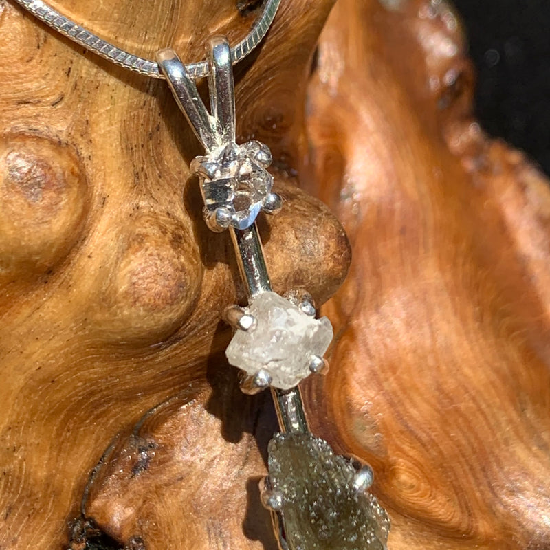 close up view of a sterling silver pendant necklace with Herkimer diamond, moldavite, and phenacite sitting on driftwood for display