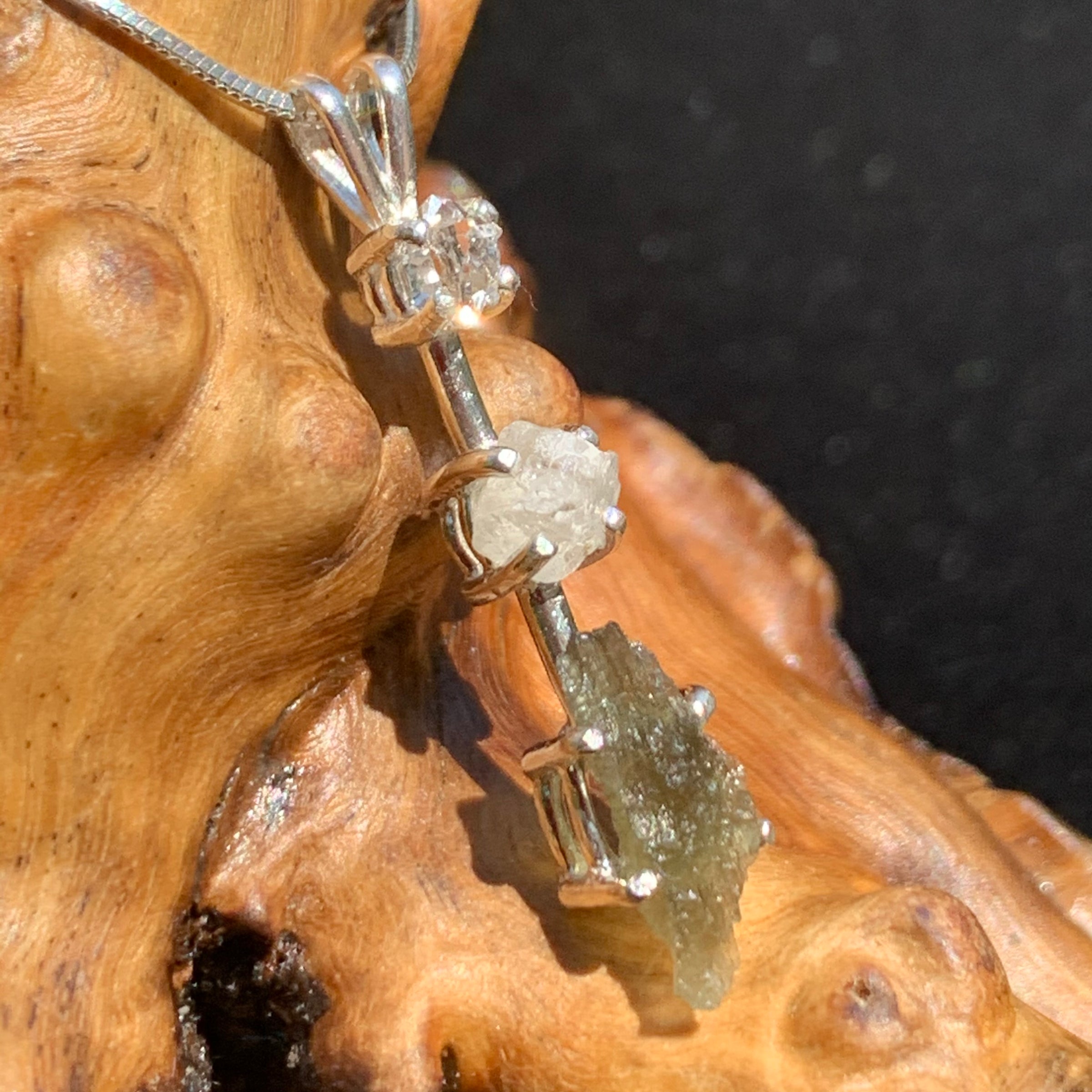 sterling silver pendant necklace with Herkimer diamond, moldavite, and phenacite sitting on driftwood for display