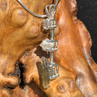 side view of a sterling silver pendant necklace with Herkimer diamond, moldavite, and phenacite sitting on driftwood for display