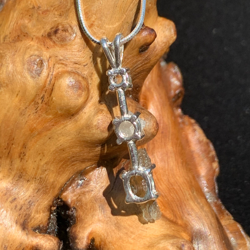 back side view of a sterling silver pendant necklace with Herkimer diamond, moldavite, and phenacite sitting on driftwood for display
