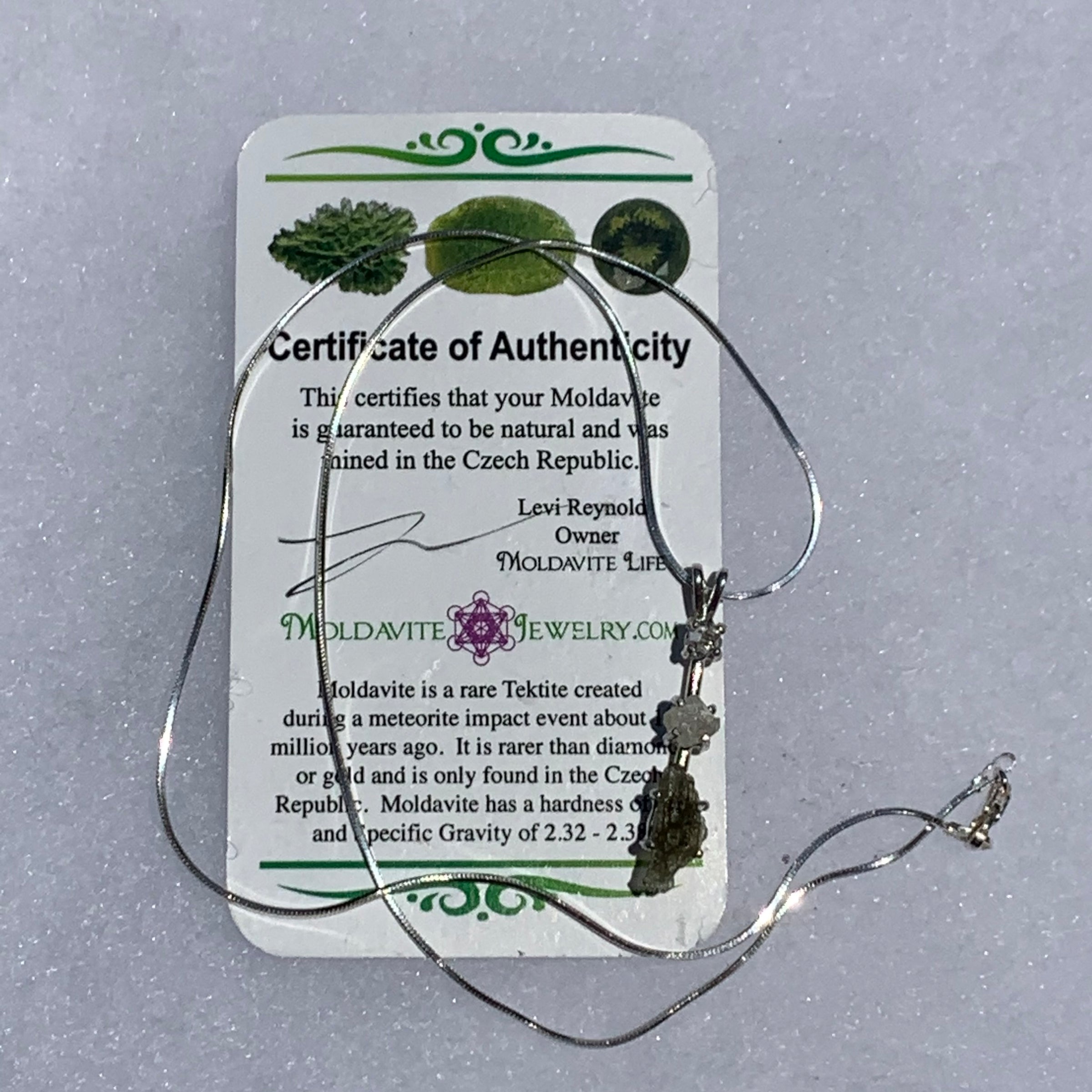 sterling silver pendant necklace with Herkimer diamond, moldavite, and phenacite sits with a moldavite life certificate of authenticity
