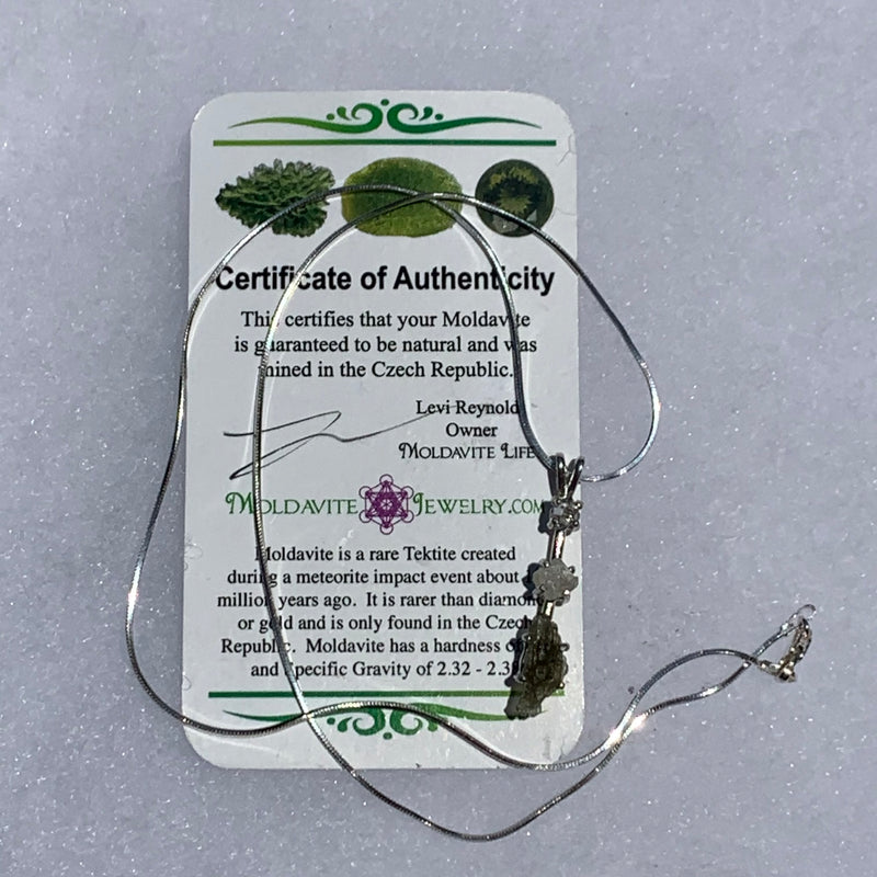 sterling silver pendant necklace with Herkimer diamond, moldavite, and phenacite sits with a moldavite life certificate of authenticity
