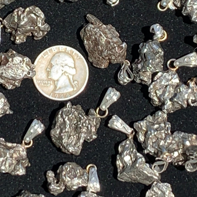 Several Campo pendants surround a US quarter on a black velvet background. 