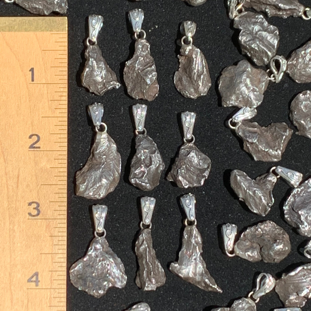 A group of Sikhote Aline meteorite pendants are set next to a ruler to show scale