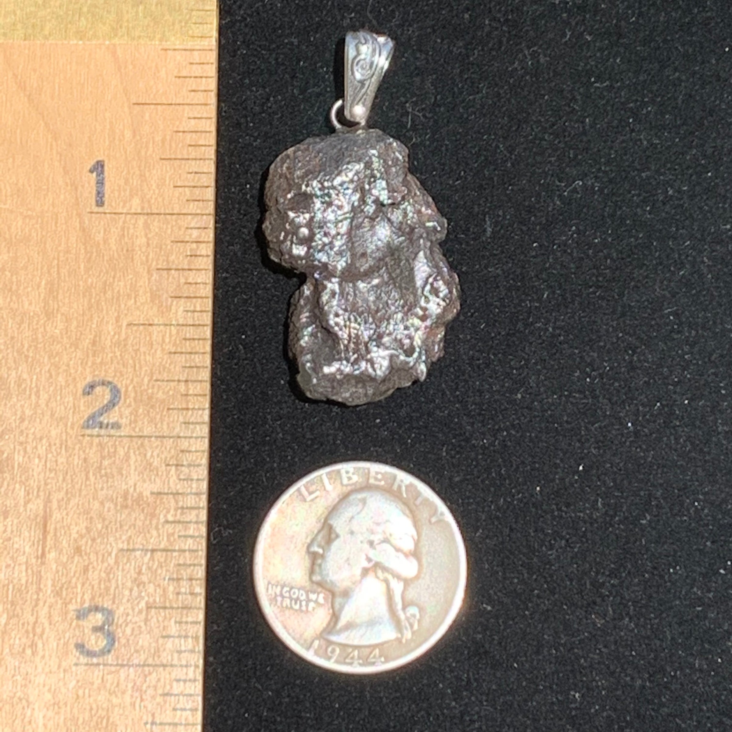 One Sikhote Aline meteorite pendant sits next to a ruler and quarter