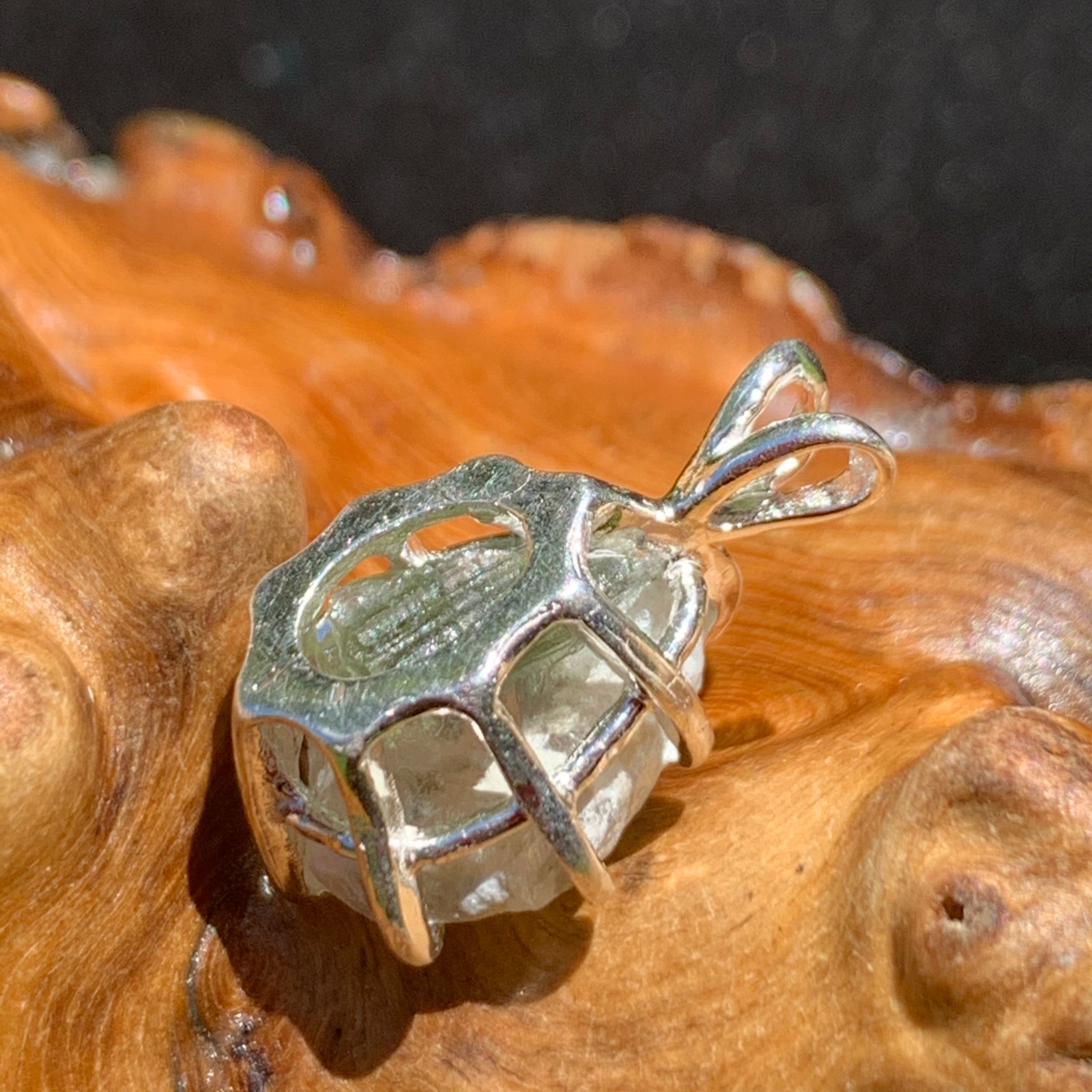 sterling silver moldavite tektite and Russian phenacite basket pendant sitting on driftwood for display