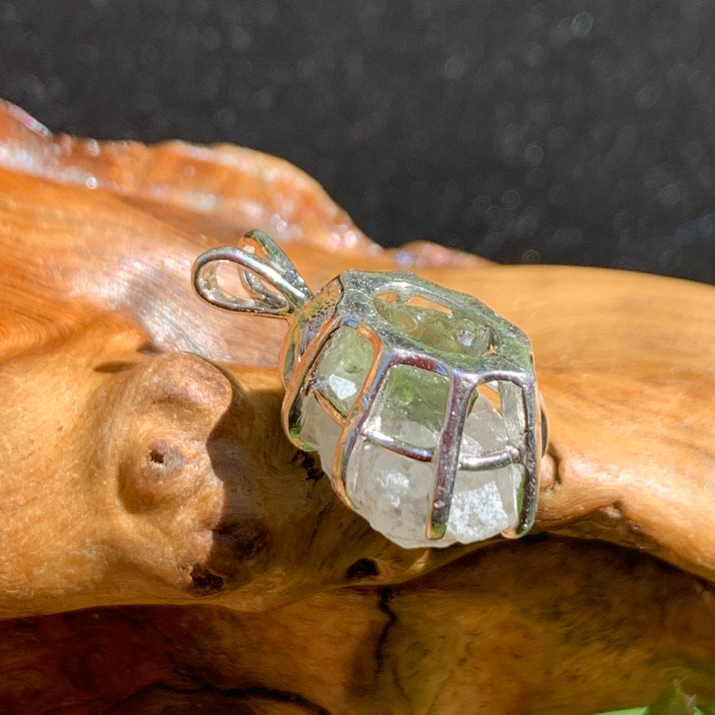 sterling silver moldavite tektite and Russian phenacite basket pendant sitting on driftwood for display