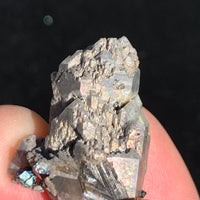 Gray quartz cluster with black brookite in matrix showing iridescent sheen while being held in hand