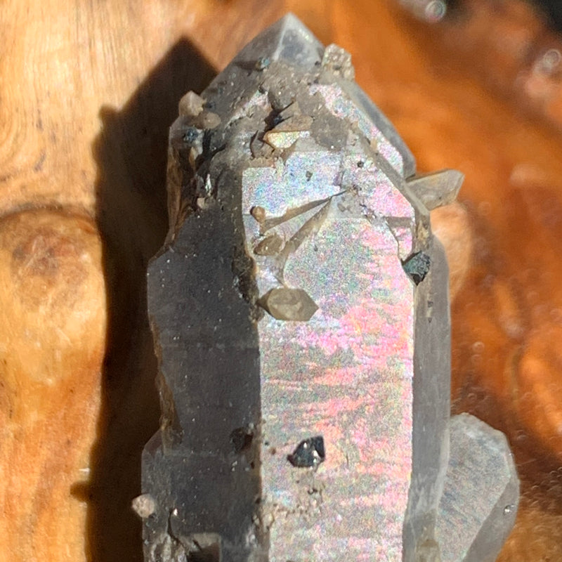 close up view of tiny brookite crystals on a smokey quartz point cluster with an iridescent sheen sitting on driftwood for display