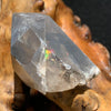 tiny brookite crystals on a smokey quartz point that's showing a rainbow light refraction inside sitting on driftwood for display