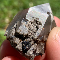 small and tiny brookite crystals on a smokey quartz point with an iridescent sheen held in hand