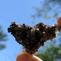 tiny brookite crystals on a smokey quartz point cluster held in hand up to the sky