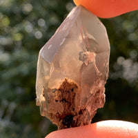 small and tiny brookite crystals on a smokey quartz point held up in hand with sunlight shining through