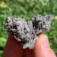 tiny brookite crystals on a smokey quartz point cluster held in hand with sunlight shining on it against a grassy background