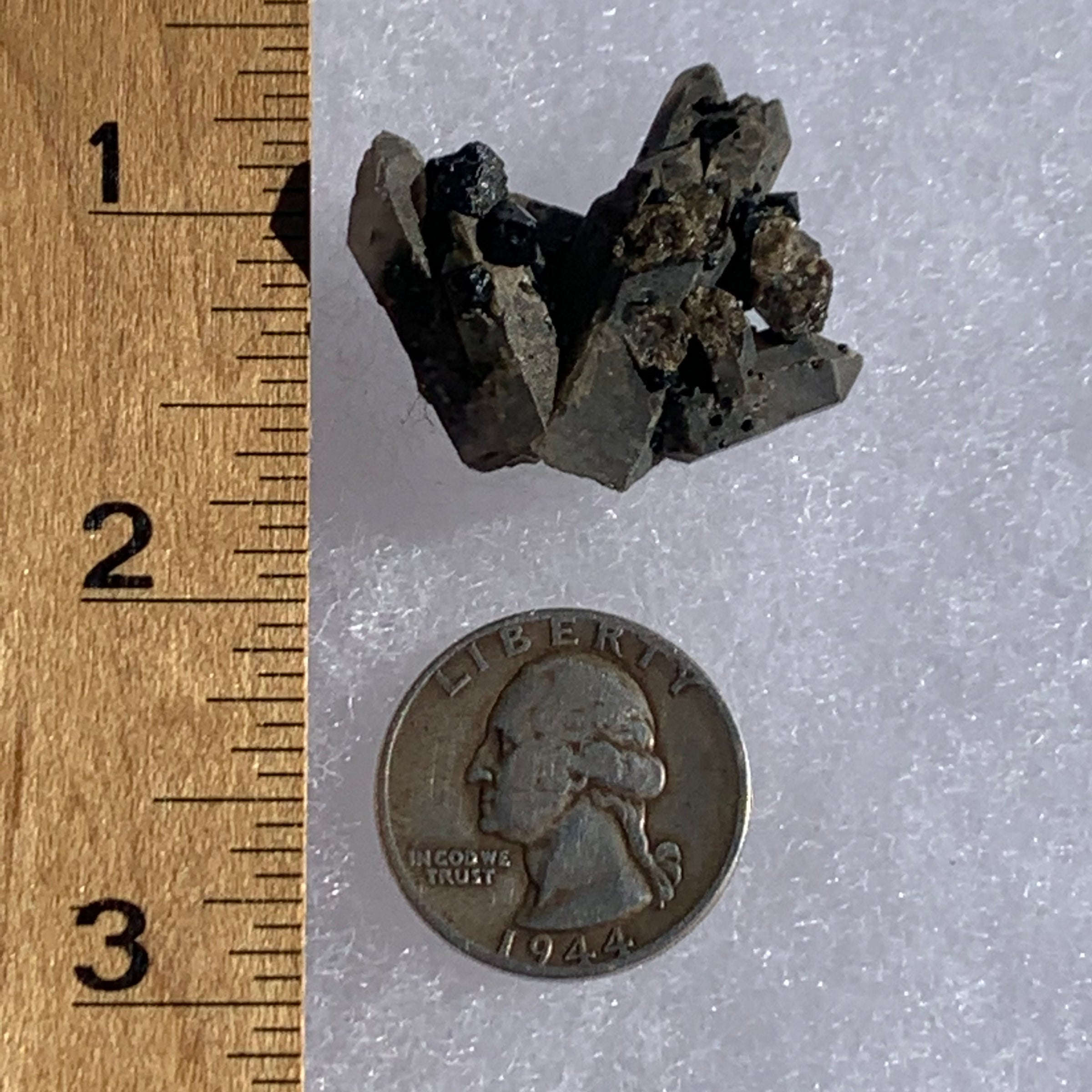big and small brookite crystals on a smokey quartz point cluster next to a ruler and a quarter for scale