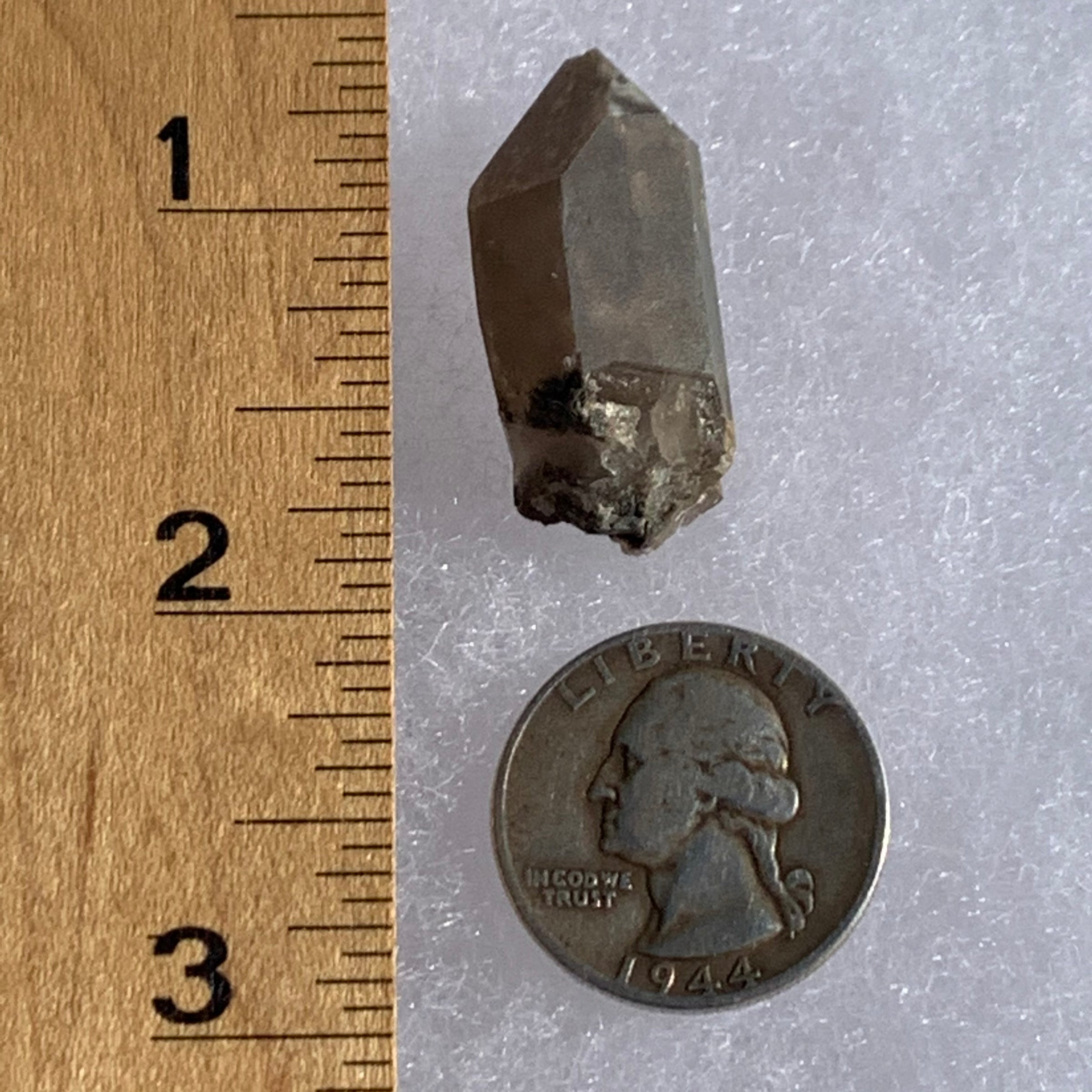 tiny brookite crystals on a terminated smokey quartz crystal next to a ruler and a quarter for scale