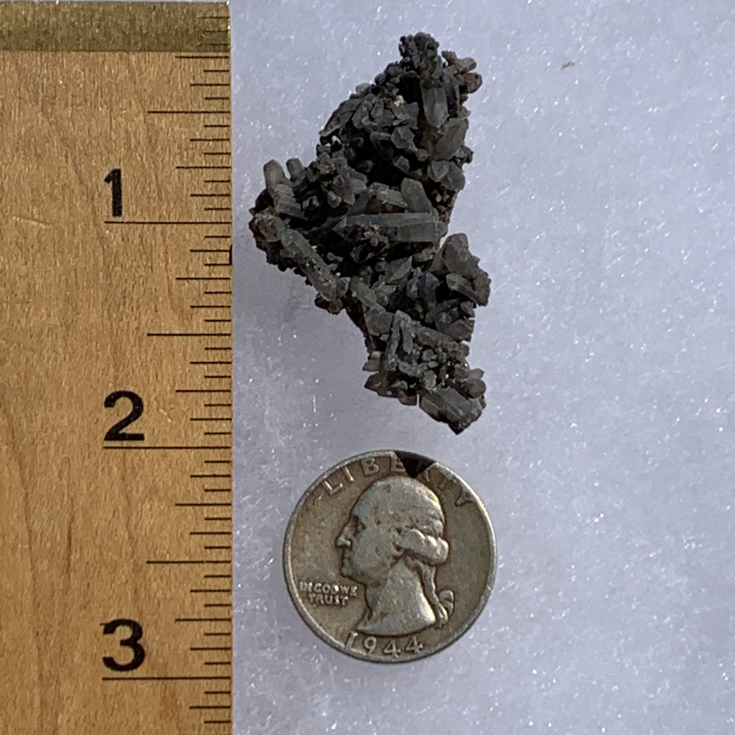 tiny brookite crystals on a smokey quartz point cluster next to a ruler and a quarter for scale