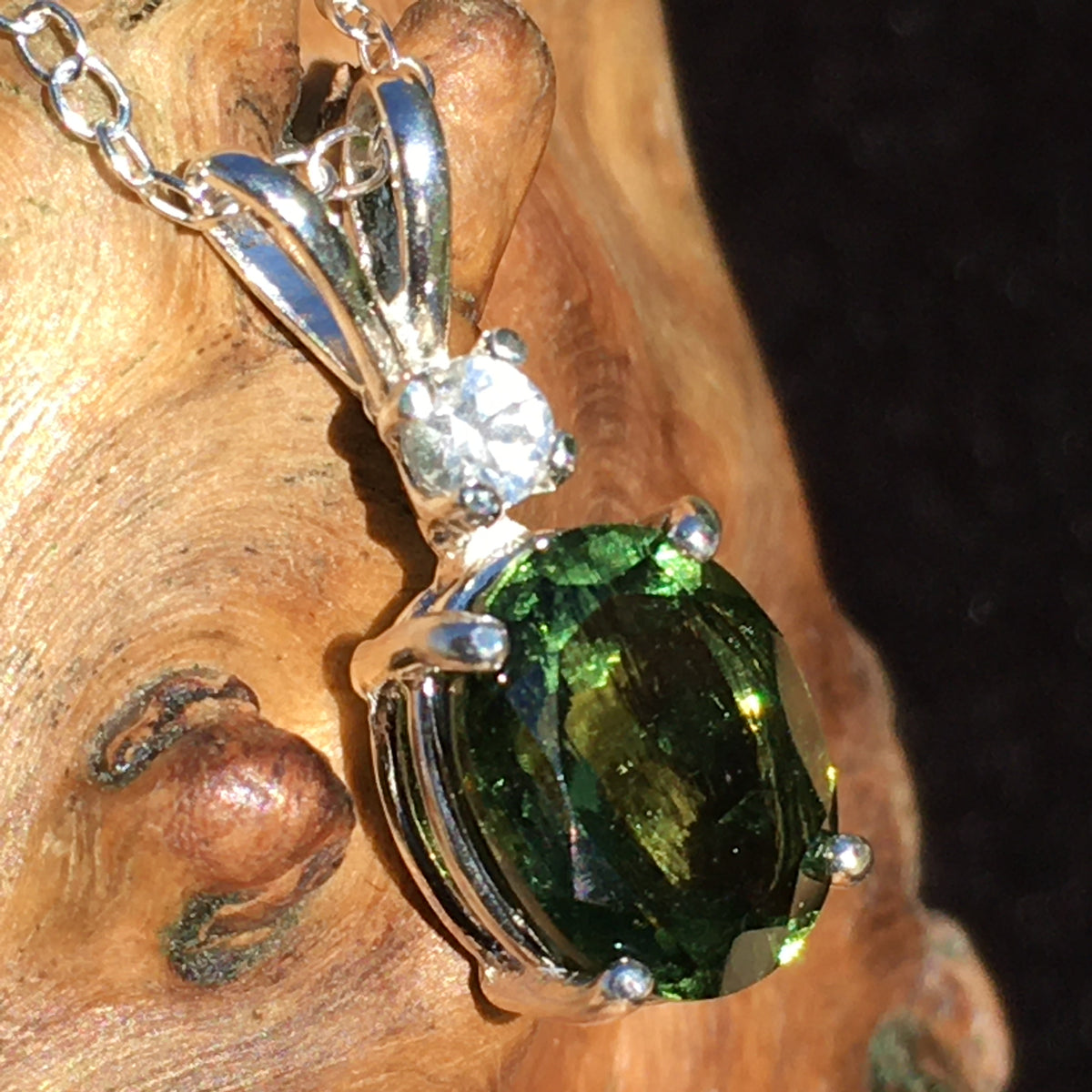 Moldavite and Brazilian phenacite pendant necklace displayed on driftwood