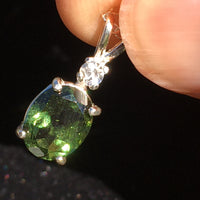 Moldavite and Brazilian phenacite pendant held in hand with light shining