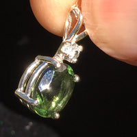 Side view of Moldavite and Brazilian phenacite pendant held in hand with light shining