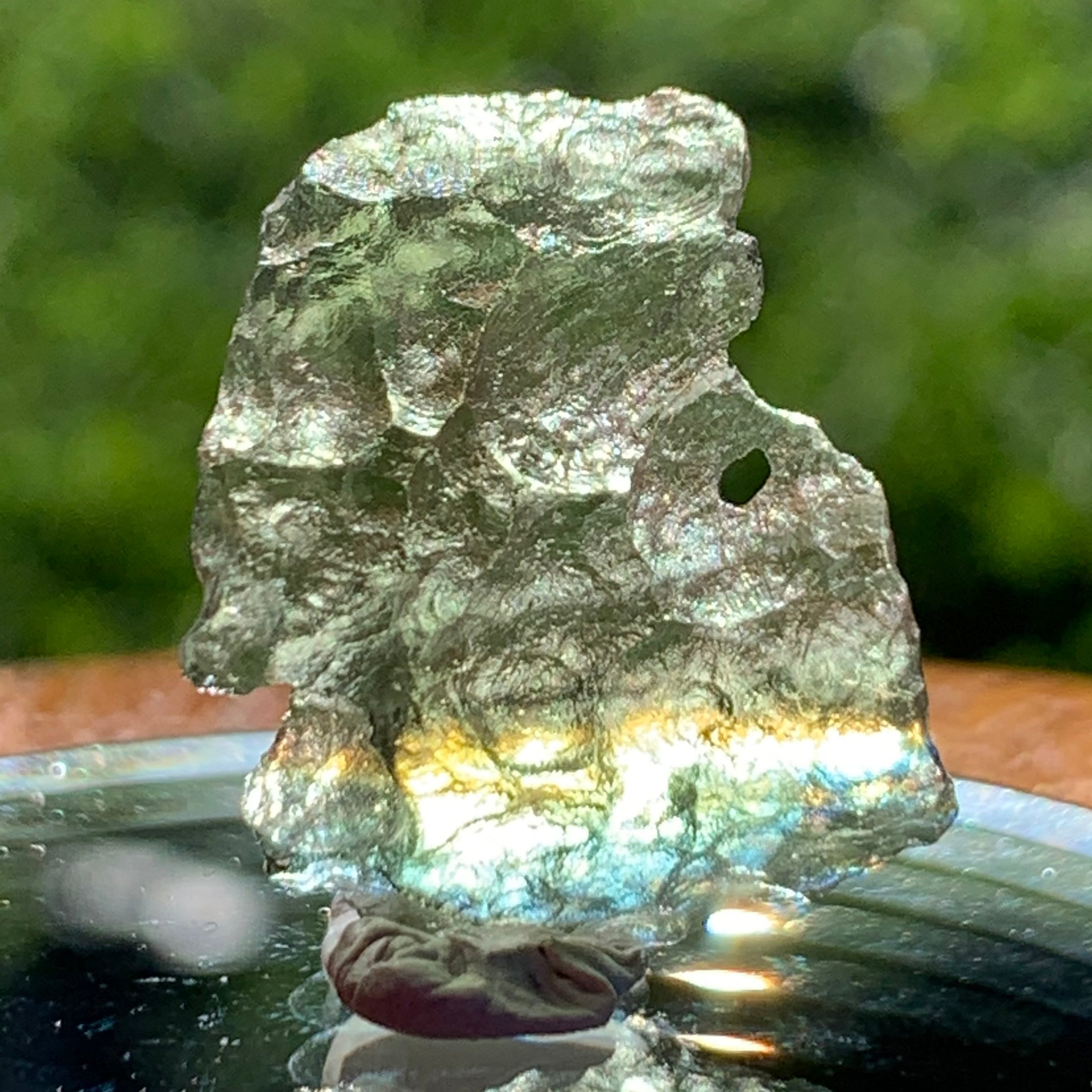 light reflects a rainbow through the thin green besednice moldavite tektite on display