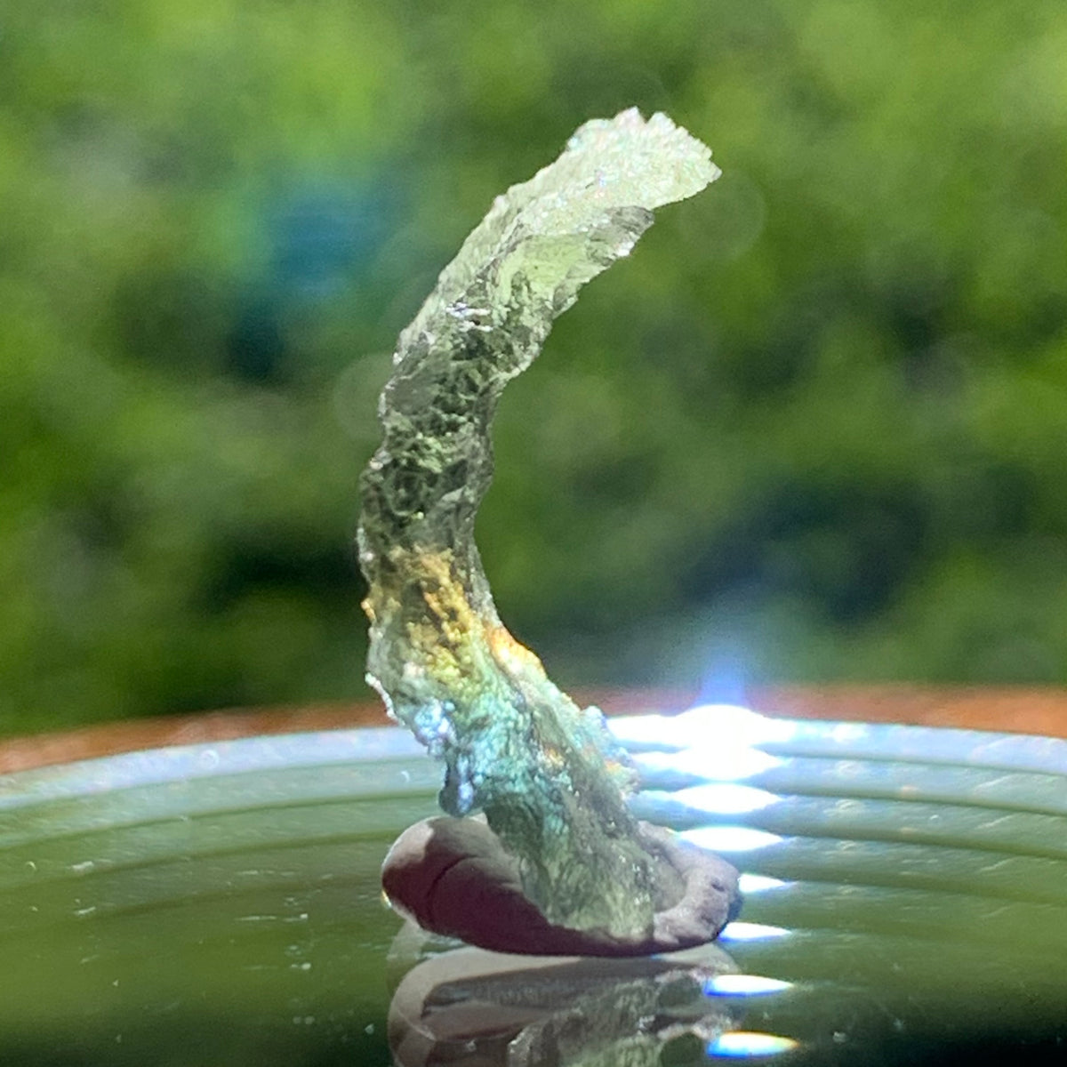 light reflects a rainbow on the thin green besednice moldavite tektite on display