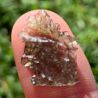 thin green besednice moldavite tektite held up on fingertips for scale