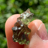 thin green besednice moldavite tektite held up on fingertips for scale