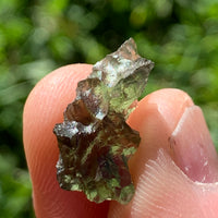 thin green besednice moldavite tektite held up on fingertips for scale
