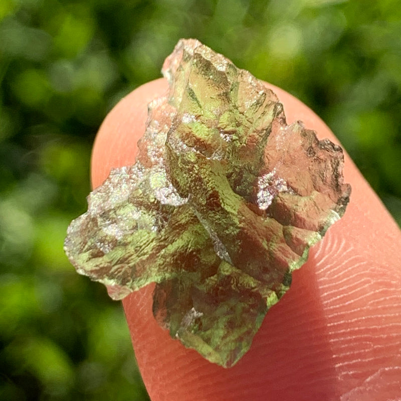 thin green besednice moldavite tektite held up on fingertips for scale