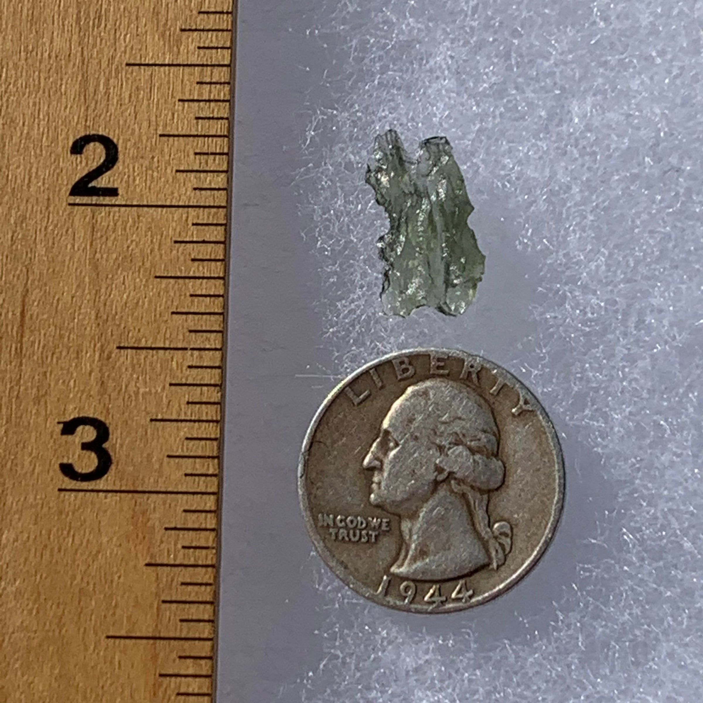 thin green besednice moldavite tektite next to a ruler and US quarter for scale