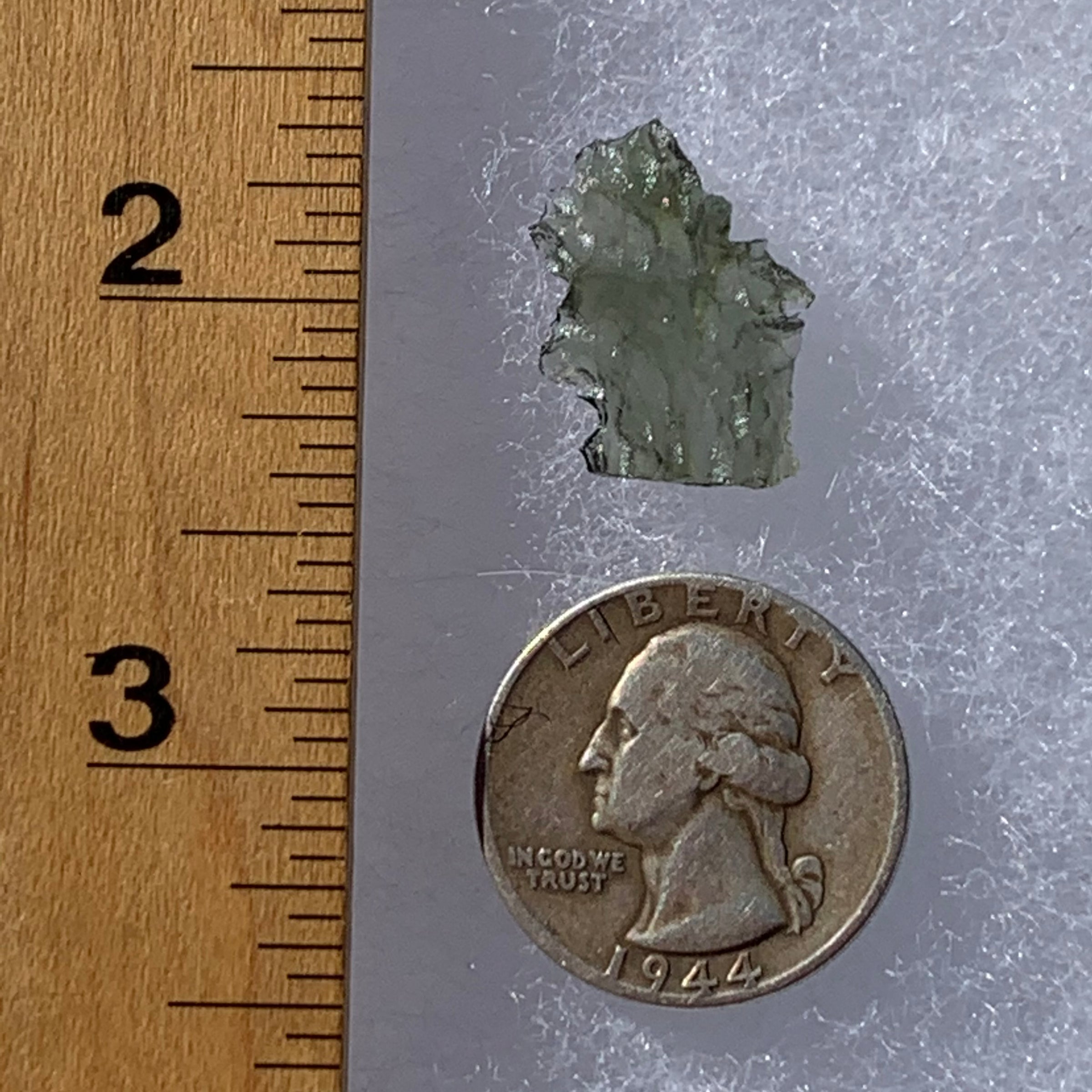 thin green besednice moldavite tektite next to a ruler and US quarter for scale