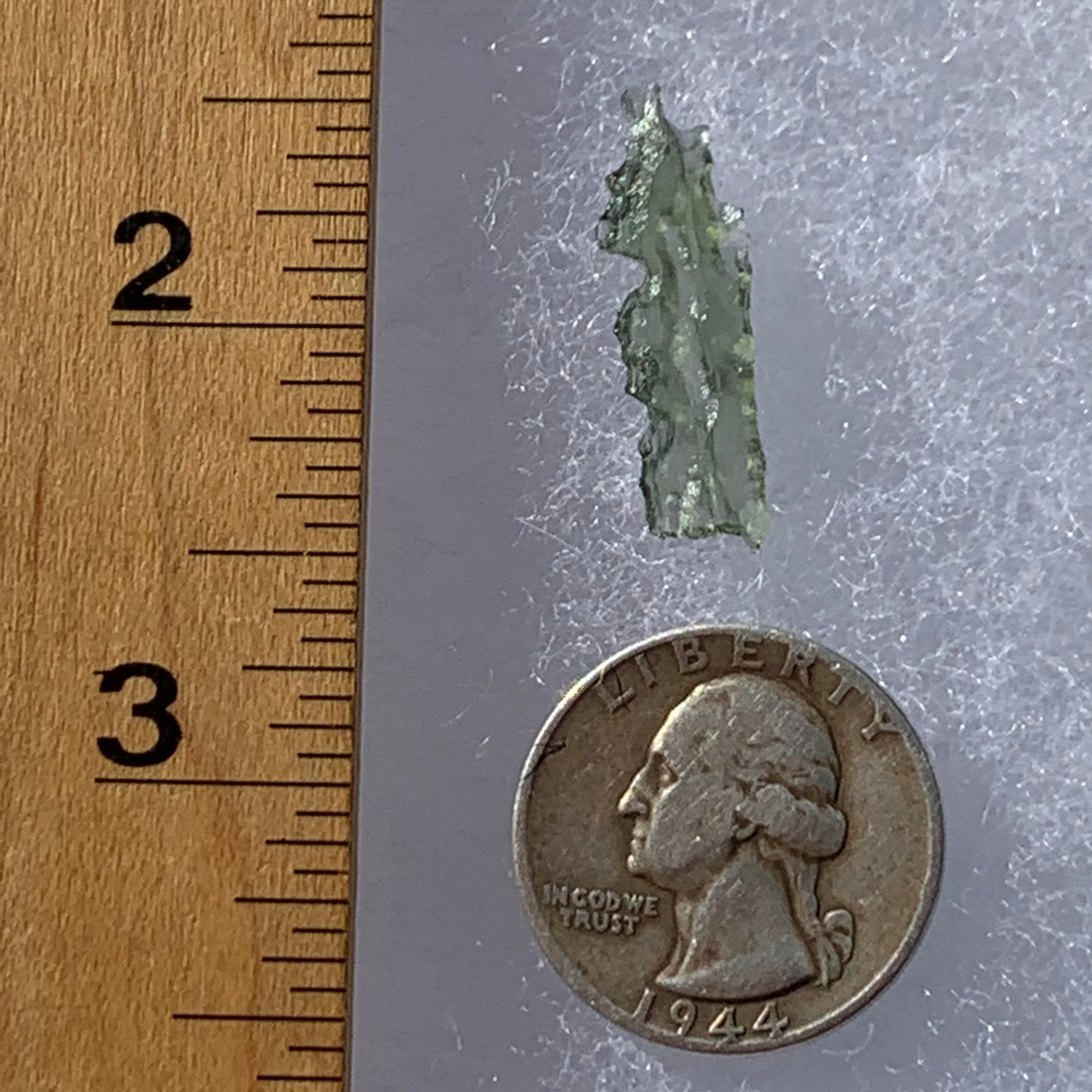 thin green besednice moldavite tektite next to a ruler and US quarter for scale