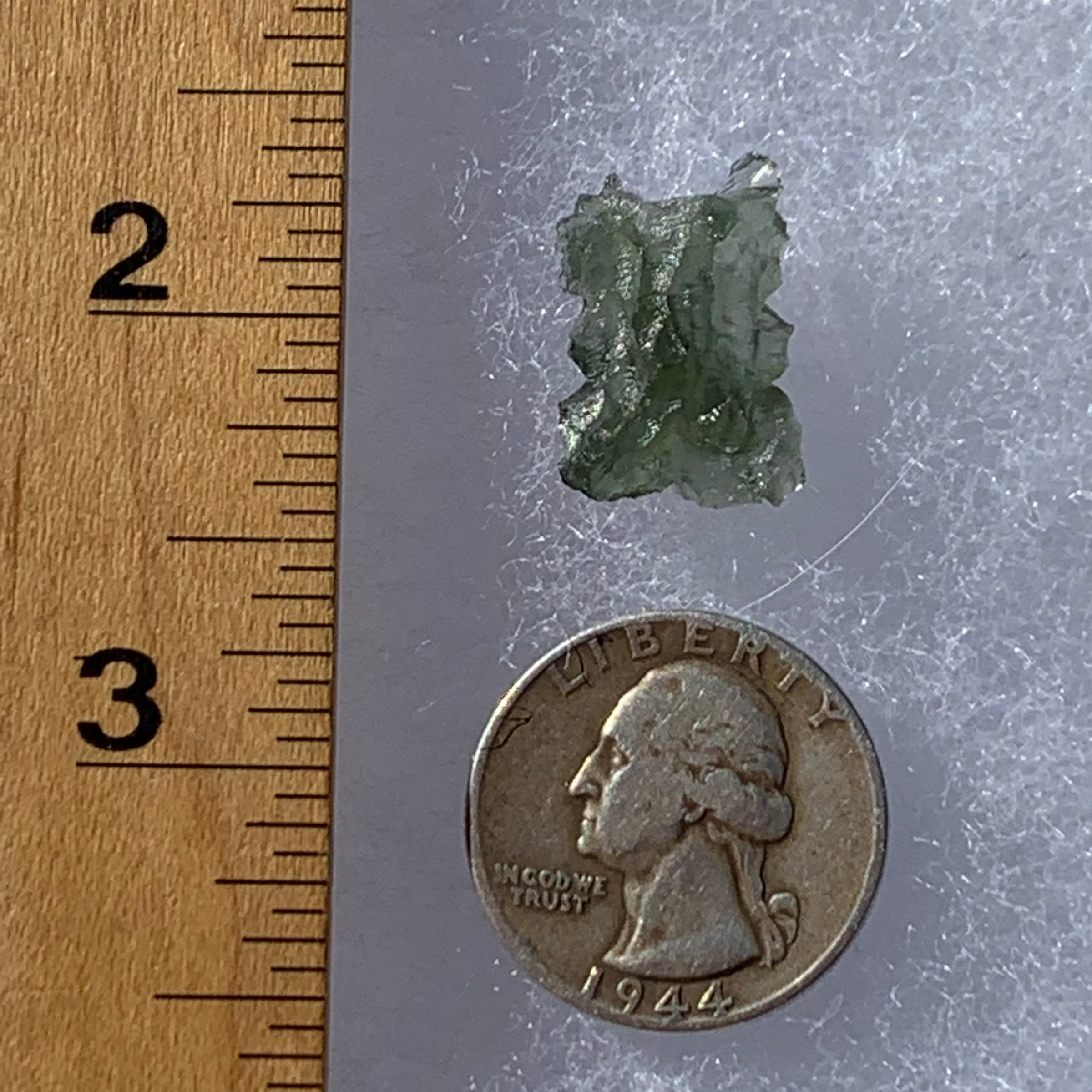 thin green besednice moldavite tektite next to a ruler and US quarter for scale