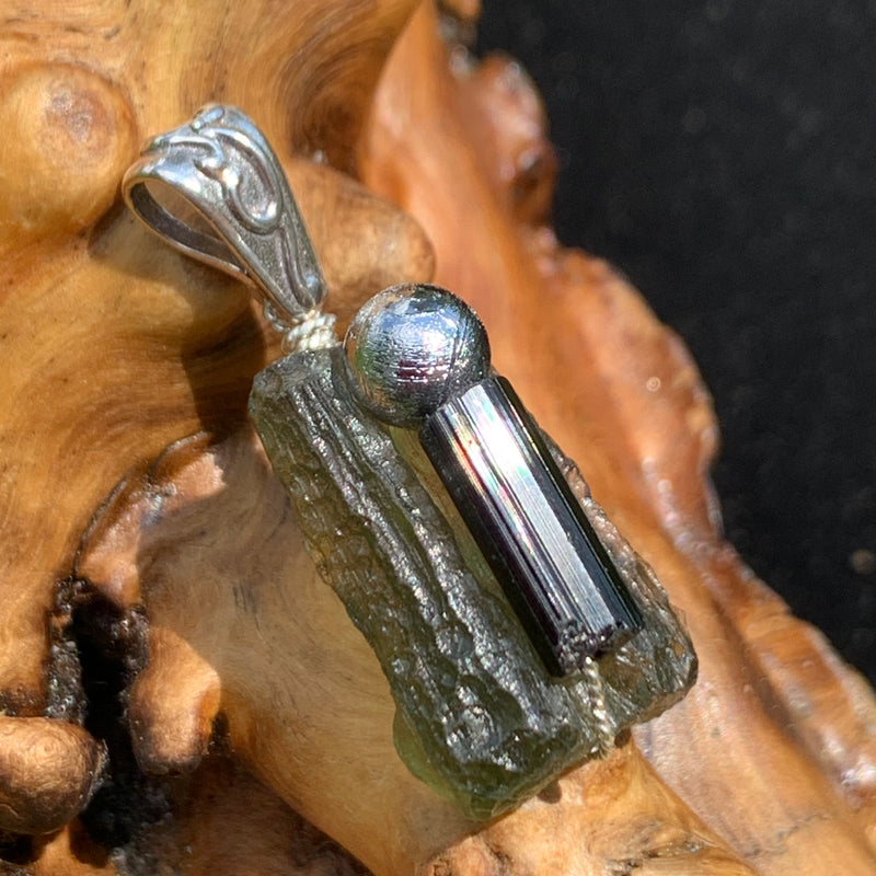 the silver moldavite tourmaline meteorite pendant sits on driftwood for display