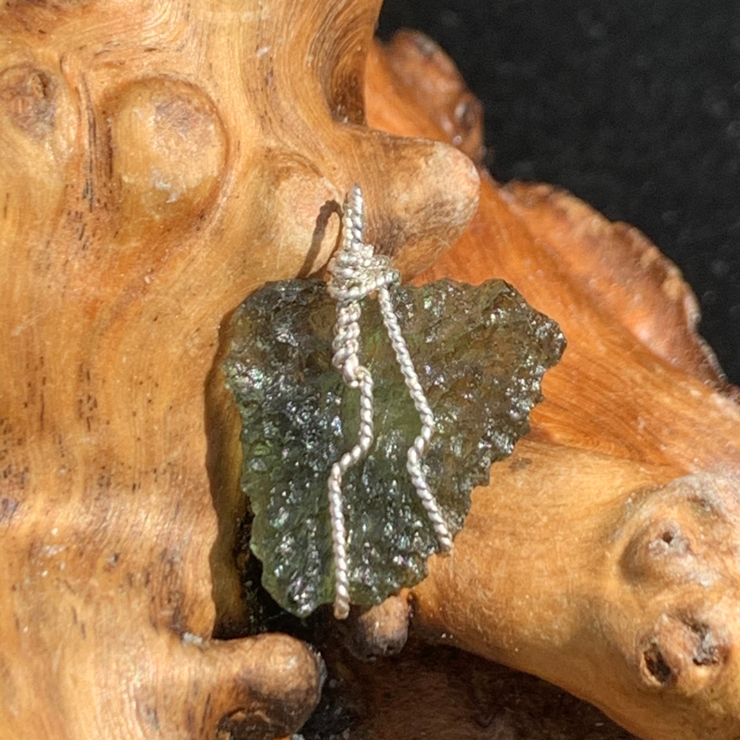 back side of sterling silver wire wrapped raw moldavite tektite and colorado phenacite crystal pendant sitting on driftwood for display