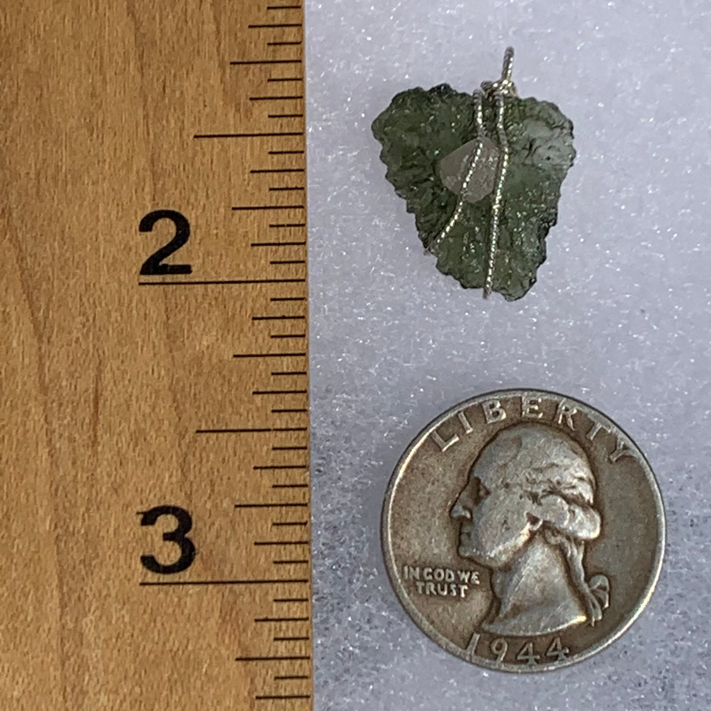 sterling silver wire wrapped raw moldavite tektite and colorado phenacite crystal pendant next to a quarter and a ruler for scale