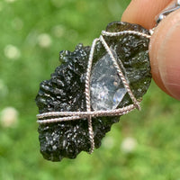 the moldavite herkimer diamond pendant is held out so it can be seen in the light