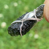 the moldavite herkimer diamond pendant is held out so it can be seen in the light with a side view