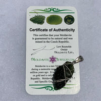 the pendant looks dark against the certificate of authenticity for the moldavite