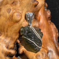 Moldavite pendant wire wrapped in sterling silver sitting on driftwood for display