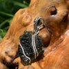 Moldavite pendant wire wrapped in sterling silver sitting on driftwood for display